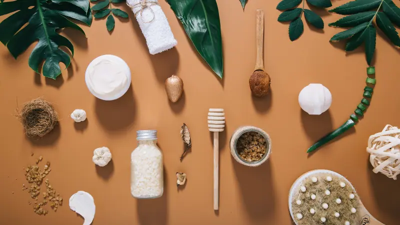 Berbagai bahan alami skincare, termasuk daun hijau, krim, madu, scrub, dan botol ramuan alami yang disusun rapi di atas latar cokelat, merepresentasikan perawatan kulit berbahan alami dan ramah lingkungan.