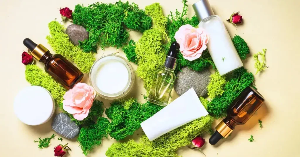 Beragam produk skincare alami, termasuk botol serum, krim, dan lotion, dikelilingi bunga mawar, lumut hijau, dan batu alami di atas latar krem, menciptakan tampilan elegan dan ramah lingkungan.